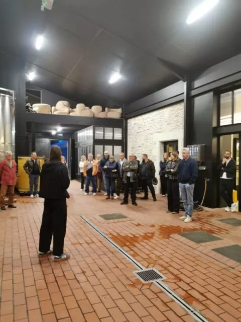 Le groupe de visiteurs dans le chai viticole, sur un sol en terre cuite, écoutant la guide.