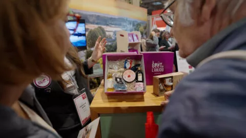 Photo de deux coffrets de produits fabriqués en Anjou exposés sur un stand. Deux personnes de dos le regarde et une troisième, face à eux, leur présente.